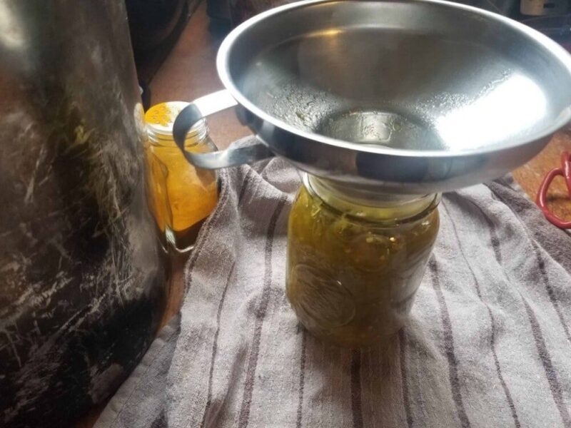 Image of canning jar full of chow chow with metal canning funnel on top.