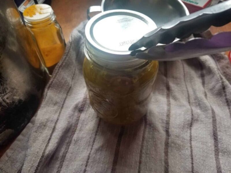 Image of canning lid being placed on jar with metal tongs.